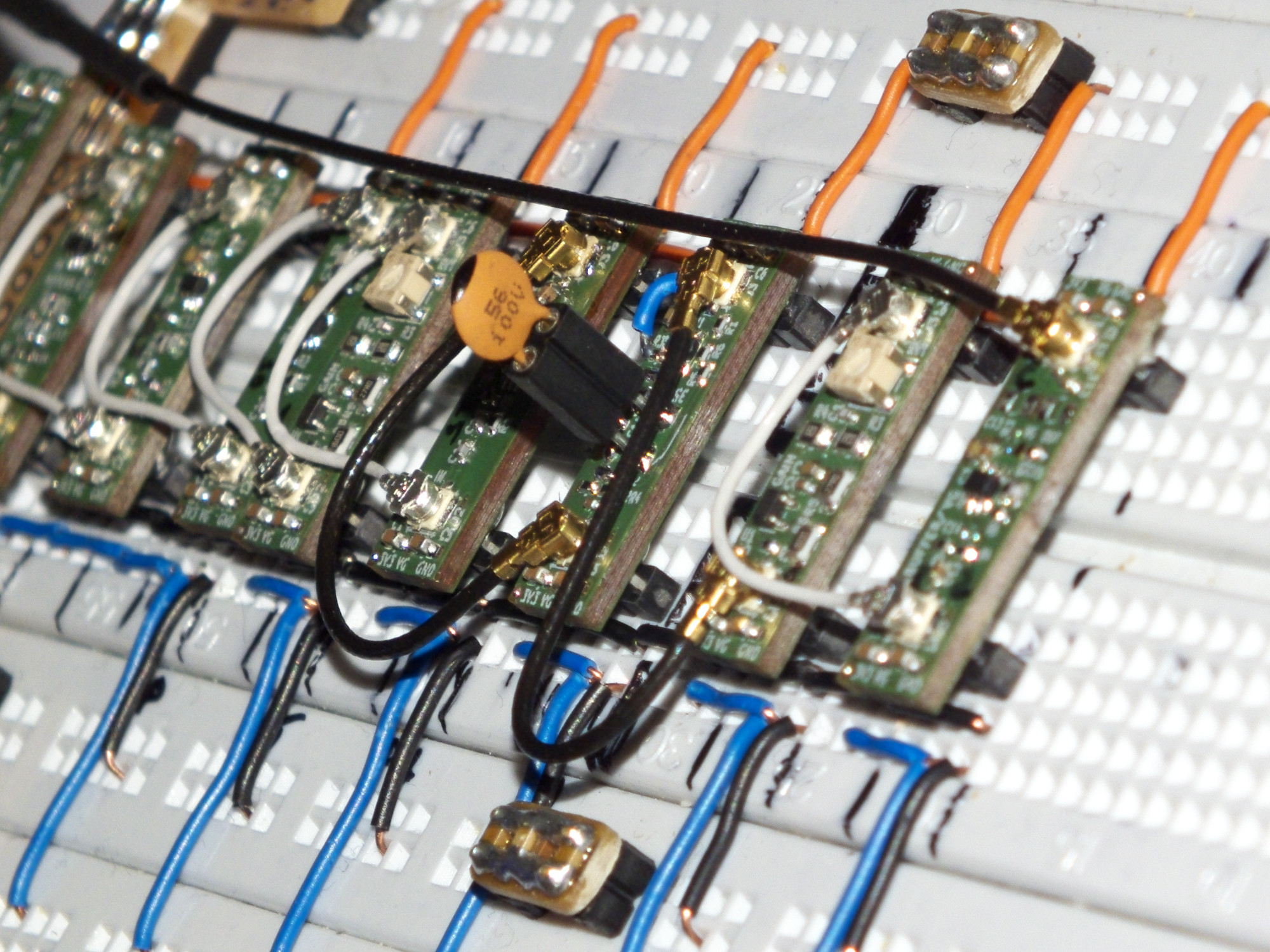 Photo of a breadboard containing eight small pcb stripes on 100 mil headers. The stripes are connected to the power rail by orange, to virtual ground by blue and to ground by black wires. The two parts of the power rails are connected by small dot matrix pcbs with bulk and decoupling caps on them. The boards are connected by U.FL cables carrying the high frequency signal. Two boards have potis and one in the middle a socket containing a 56p tht caramic cap.