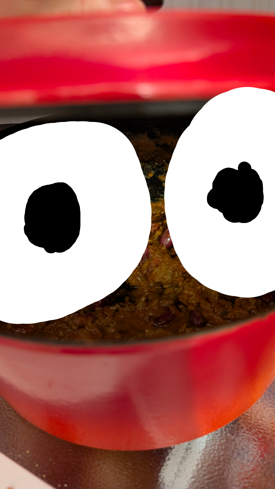 Photo of a red pot of chilli the lid is just opened slightly to photograph the inside. Two big eyes have been drawn in the opening.