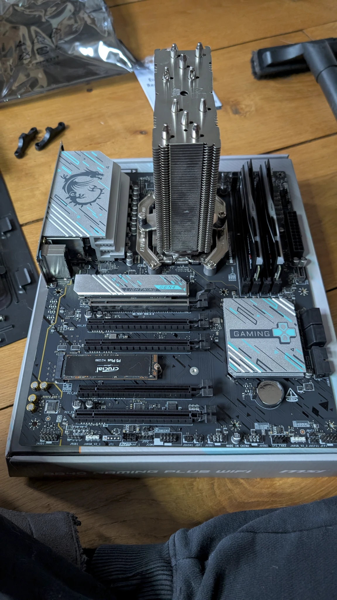 Photo of a motherboard sittin gon a box, with RAM and a CPU cooler attached. Presumably there's a CPU under that cooler too, who knows.