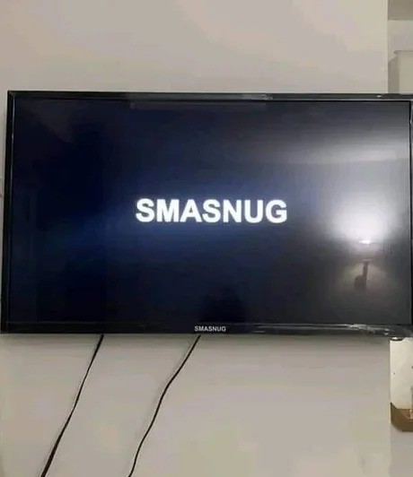 a picture of a tv hanging at a wall, with its boot animation saying "smasnug" instead of samsung, likely because of it being a knock off samsung tv.