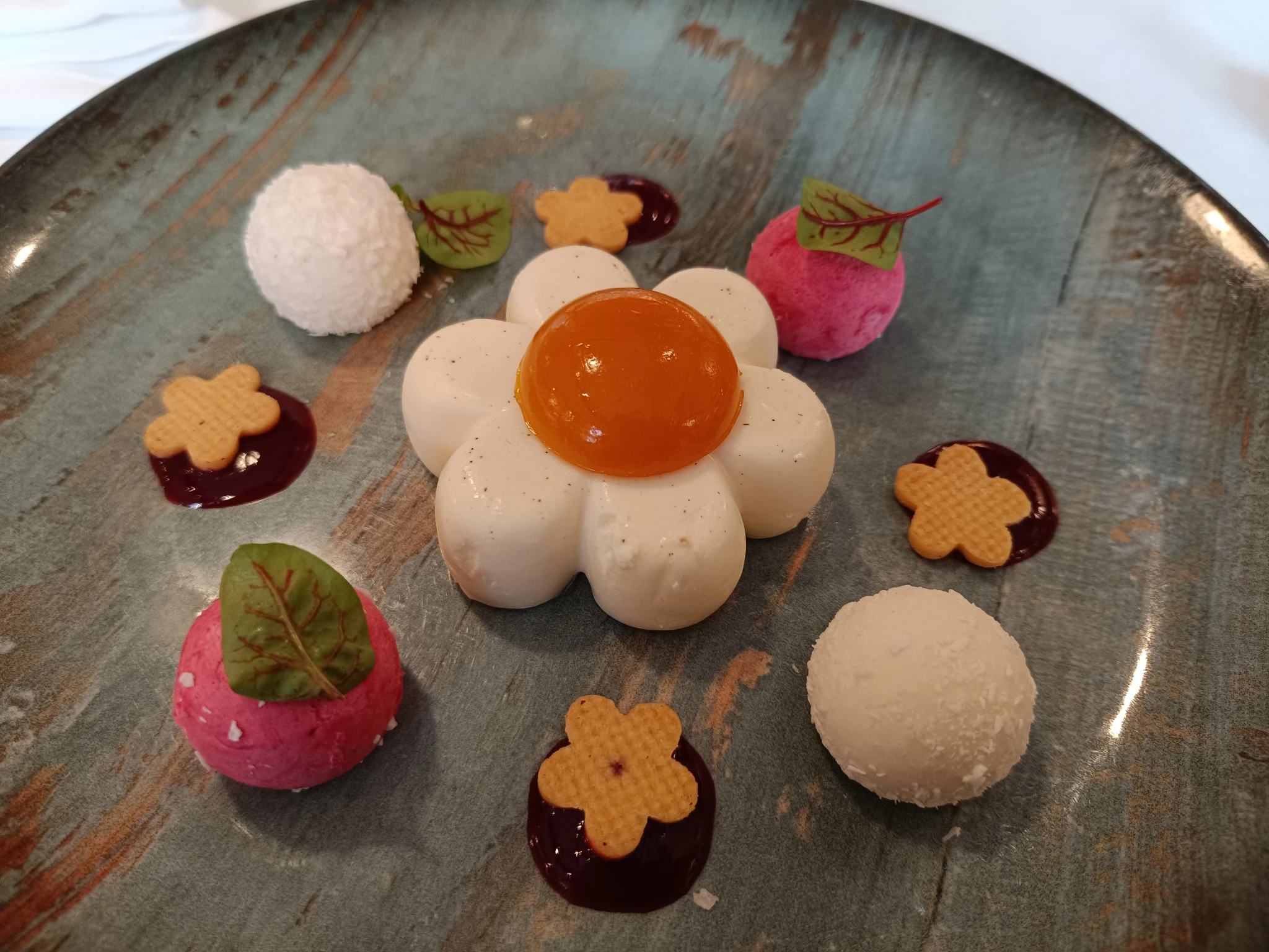 Pannacotta with the shape of a daisy flower, with some small ice cream balls with leaves on top and some tiny flower shaped cookies