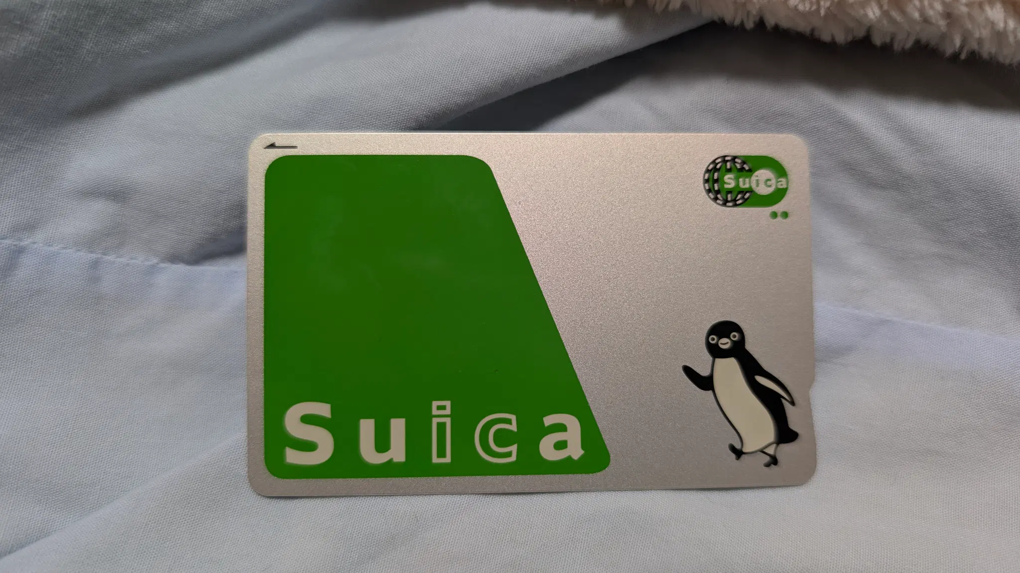 Photo of a Suica card, a silver and green card the size of a normal credit card, there's a penguin on it.
